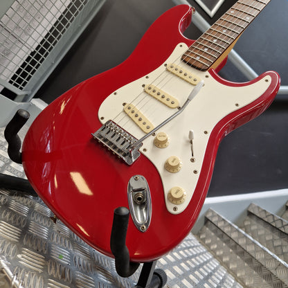 Pre-Owned Squier MIK 1992 A red electric guitar with a cream pickguard and cream knobs, resting on a stand in a workshop setting.