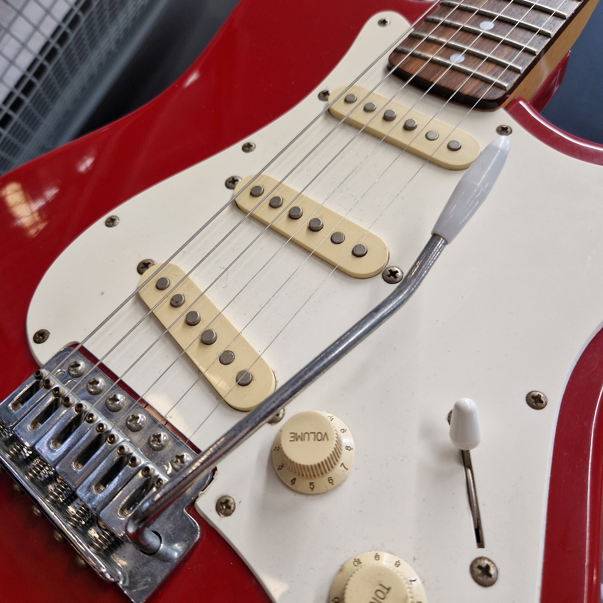 Pre-Owned Squier MIK 1992 Close-up of a red electric guitar body with a white pickguard, cream humbucker pickups, a chrome bridge, and a volume knob.