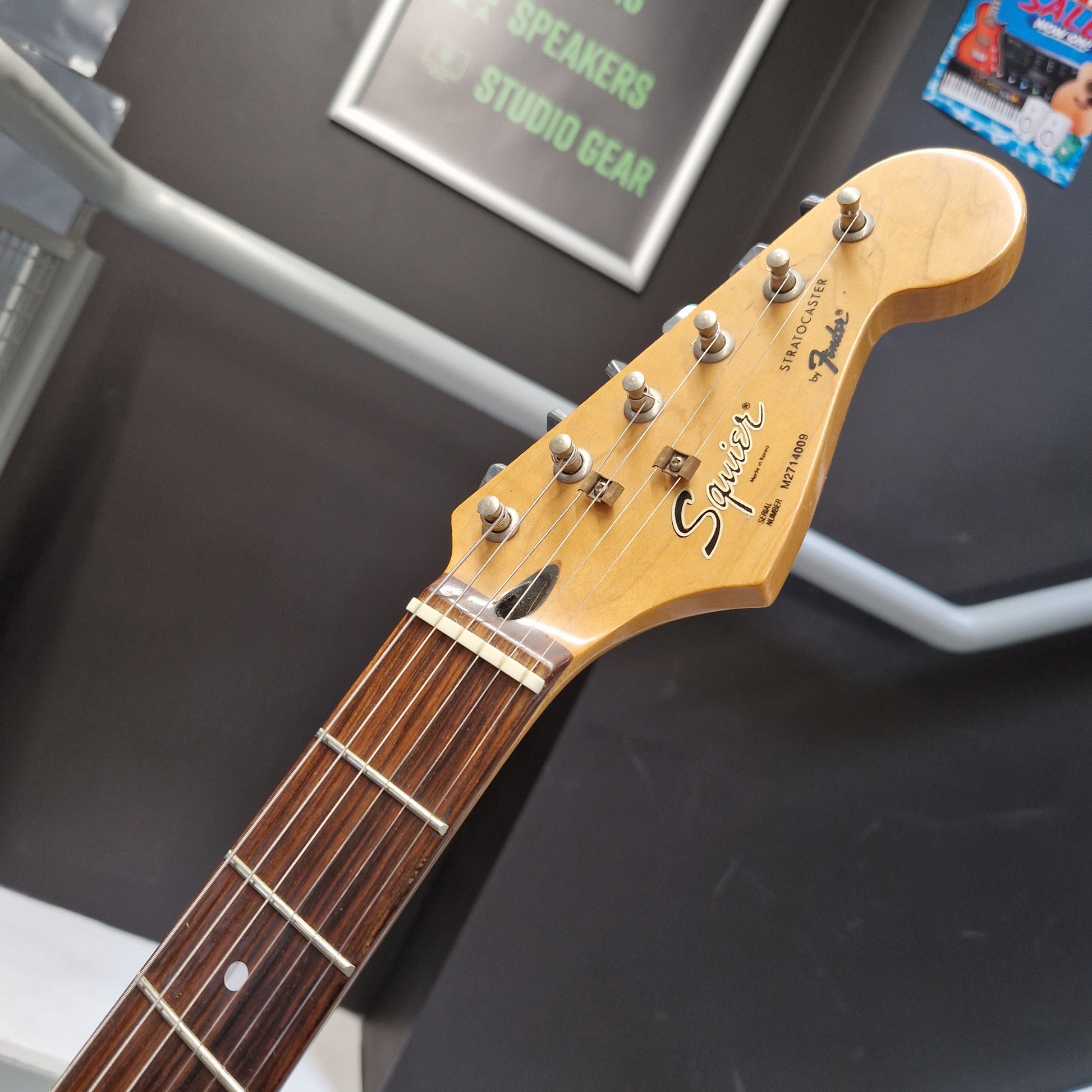 Pre-Owned Squier MIK 1992 Close-up of a Fender Stratocaster electric guitar headstock, showing the maple wood neck, six tuning pegs, and the Fender logo and 'Stratocaster' script on a dark display surface.