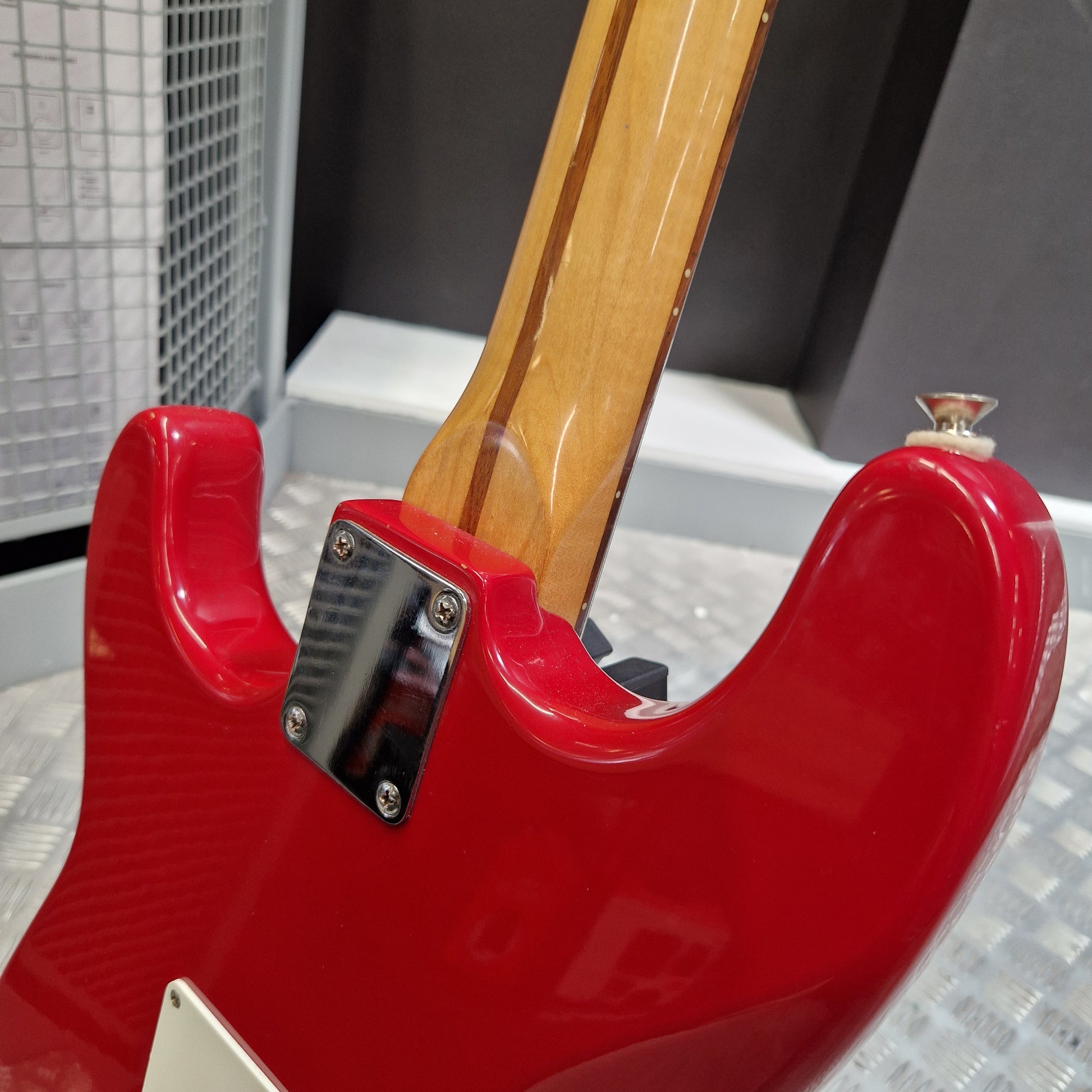 Pre-Owned Squier MIK 1992 Close-up of the rear body of a glossy red electric guitar with a natural wood neck and a black hardware plate, shown in an indoor setting.