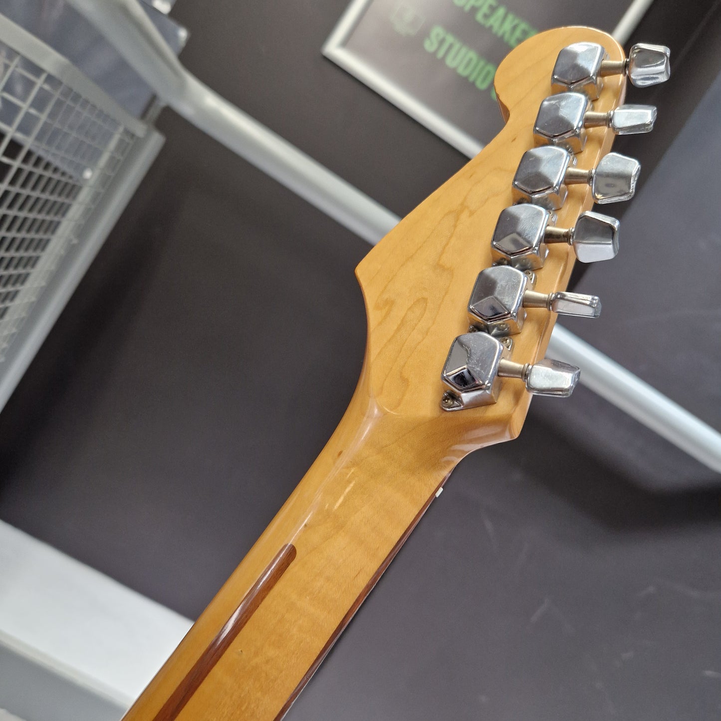 Pre-Owned Squier MIK 1992 Close-up of the headstock of an electric guitar with a natural maple wood finish and six silver tuning pegs, set against a dark gray background.