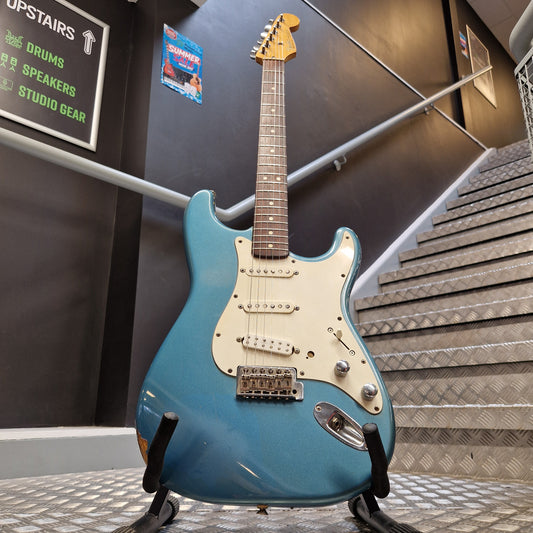 Pre-Owned Fender Mexican Stratocaster 1993 Electric - Lake Placid Blue A blue electric guitar with a white pickguard and chrome hardware, photographed hanging against a textured wall in an indoor showroom or studio space.