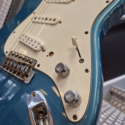 Pre-Owned Fender Mexican Stratocaster 1993 Electric - Lake Placid Blue Close-up of a blue electric guitar body with a cream pickguard, chrome control knobs, and a bridge, photographed indoors with a blurred background.