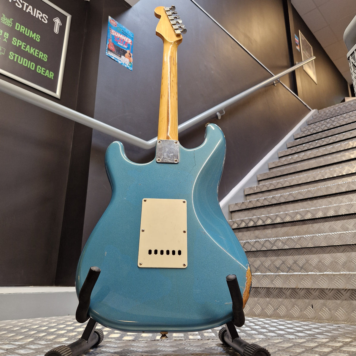 Pre-Owned Fender Mexican Stratocaster 1993 Electric - Lake Placid Blue A blue electric guitar with a natural wood neck and a cream pickguard, displayed on a stand inside what appears to be a showroom or studio.