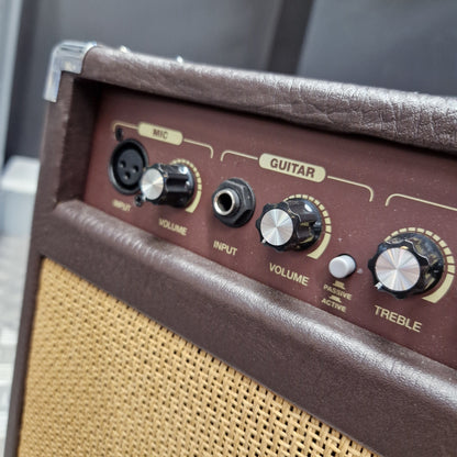 Pre-Owned Carlsbro Sherwood 20R Close-up of a brown leather-covered guitar amplifier control panel with black and silver knobs, including treble, volume, and input jacks, next to a beige woven speaker grille.