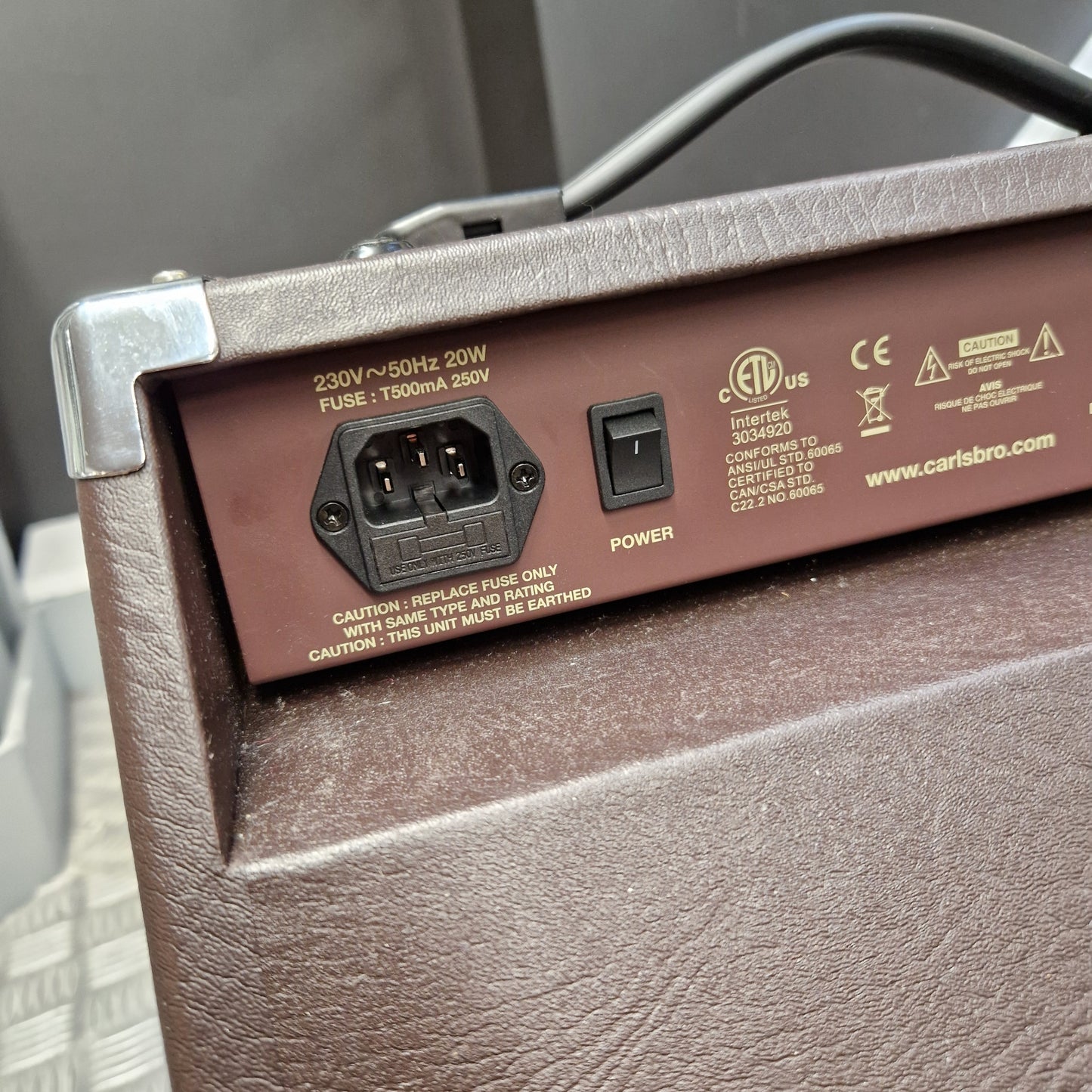 Pre-Owned Carlsbro Sherwood 20R Close-up of the rear power supply panel of a brown textured speaker or amplifier, showing a single switch labeled POWER and a 200W AC/DC power outlet, with UL certification marks and website text printed on it.