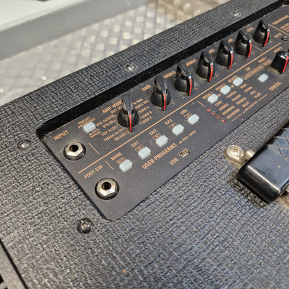 Pre-Owned Vox VT100X Close-up of a black guitar amplifier control panel with multiple knobs, white labels, and red accents on a dark textured cabinet surface.