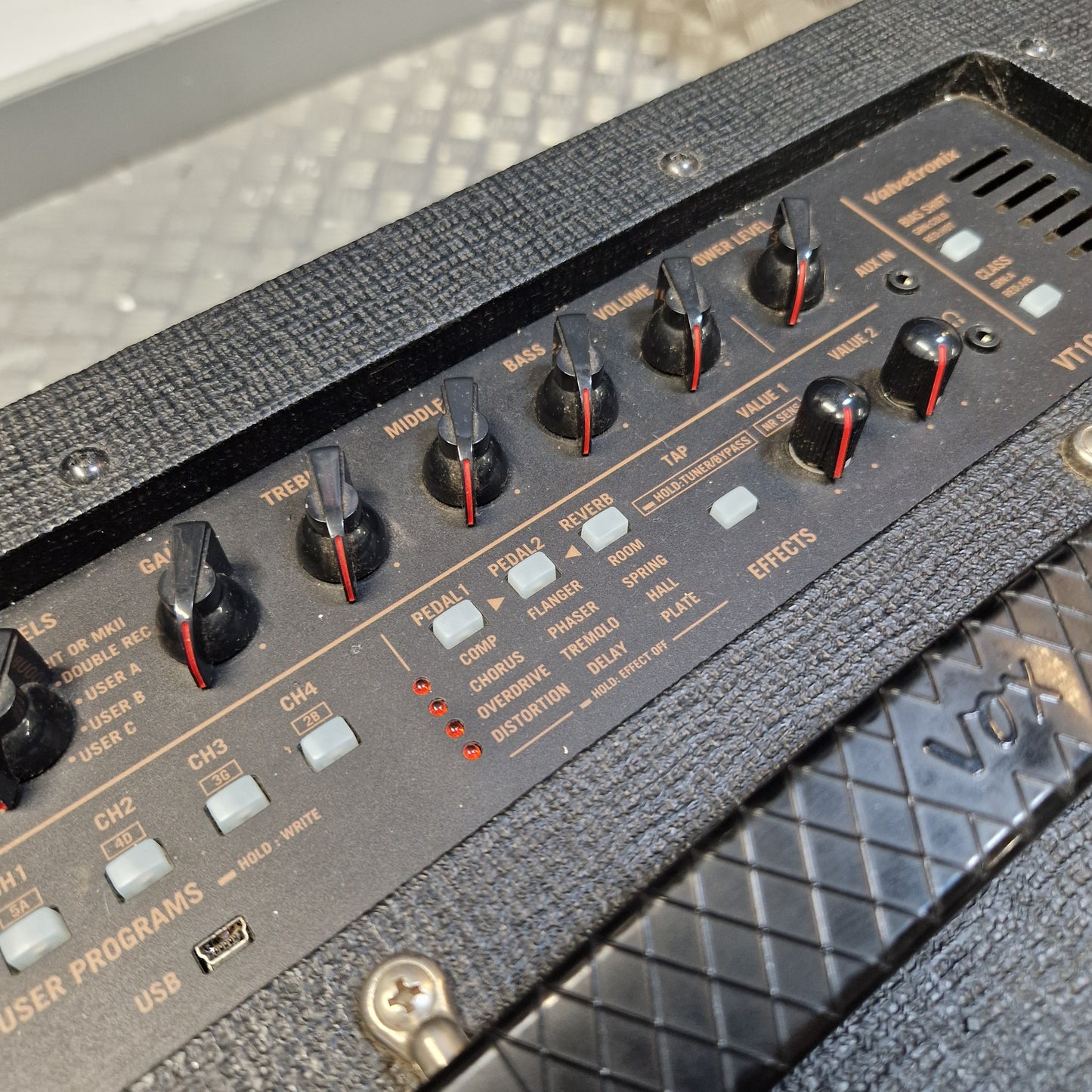 Pre-Owned Vox VT100X Close-up of a black guitar amplifier control panel with multiple rotary knobs, white switches, and gold lettering on a textured gray cabinet.