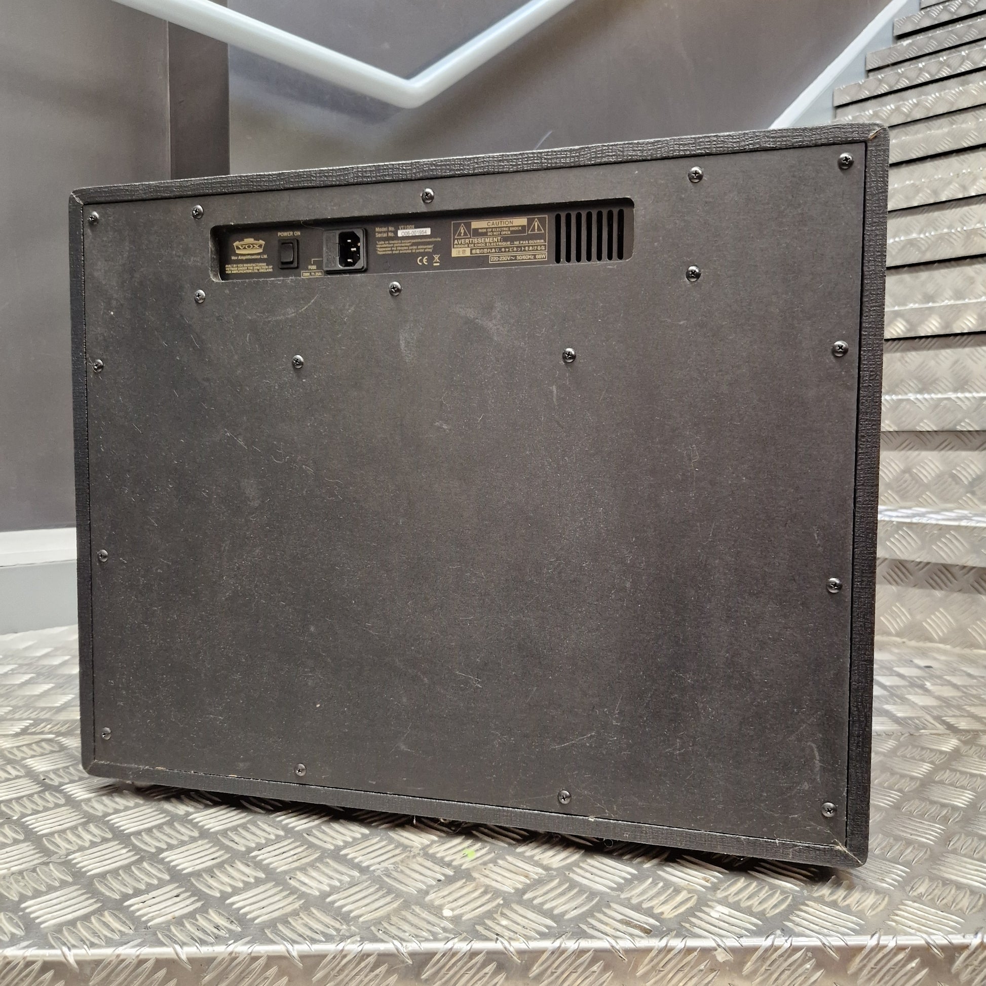 Pre-Owned Vox VT100X The rear view of a black vintage Marshall speaker cabinet resting on a diamond plate metal surface.