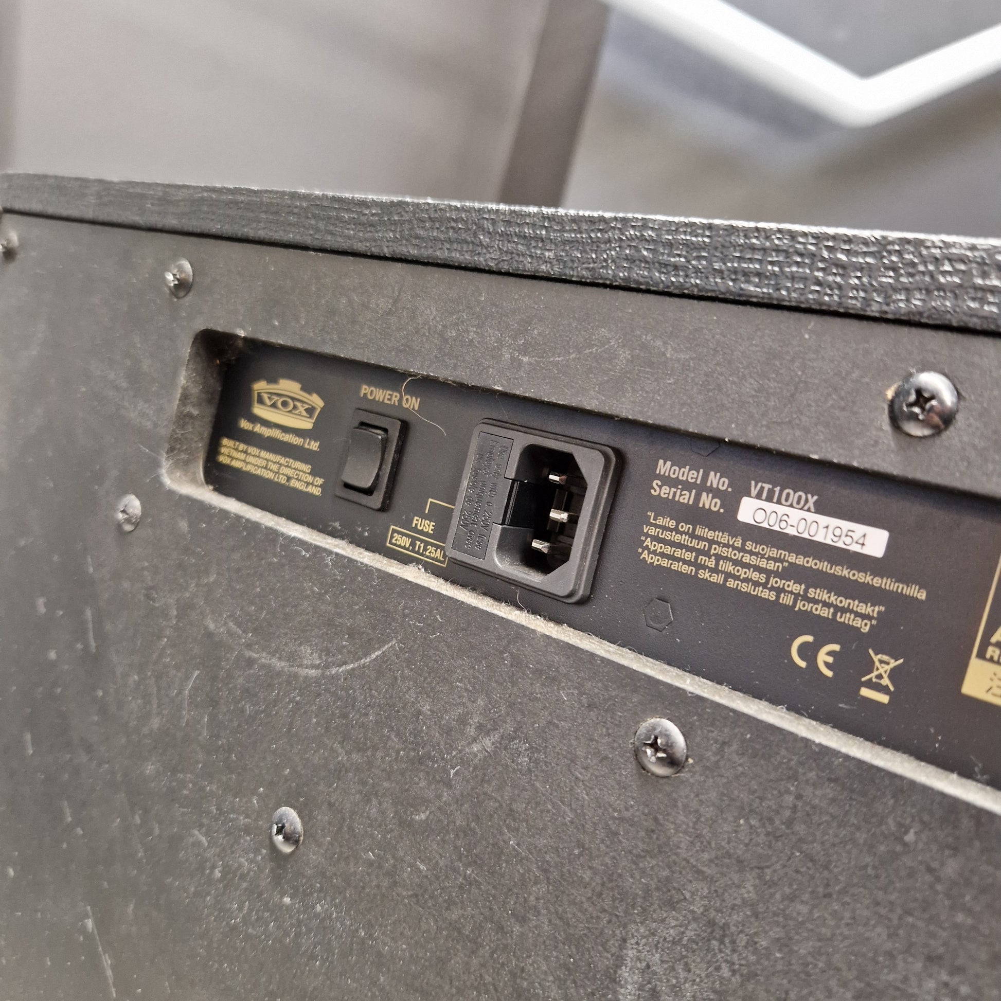 Pre-Owned Vox VT100X Close-up of the rear power supply panel of a black speaker, showing a IEC power inlet, a power switch, and printed specifications and certification marks.