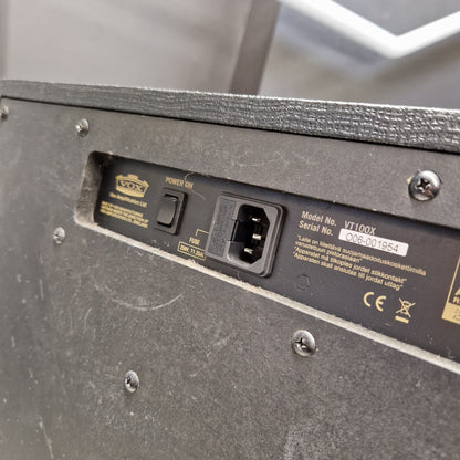 Pre-Owned Vox VT100X Close-up of the rear power supply panel of a black speaker, showing a IEC power inlet, a power switch, and printed specifications and certification marks.