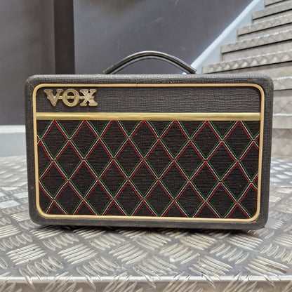 Pre-Owned Vox Escort A Vox portable speaker with a textured dark gray fabric cover, featuring a black diamond-patterned grille with red and green stitching, gold trim, and the gold Vox logo.
