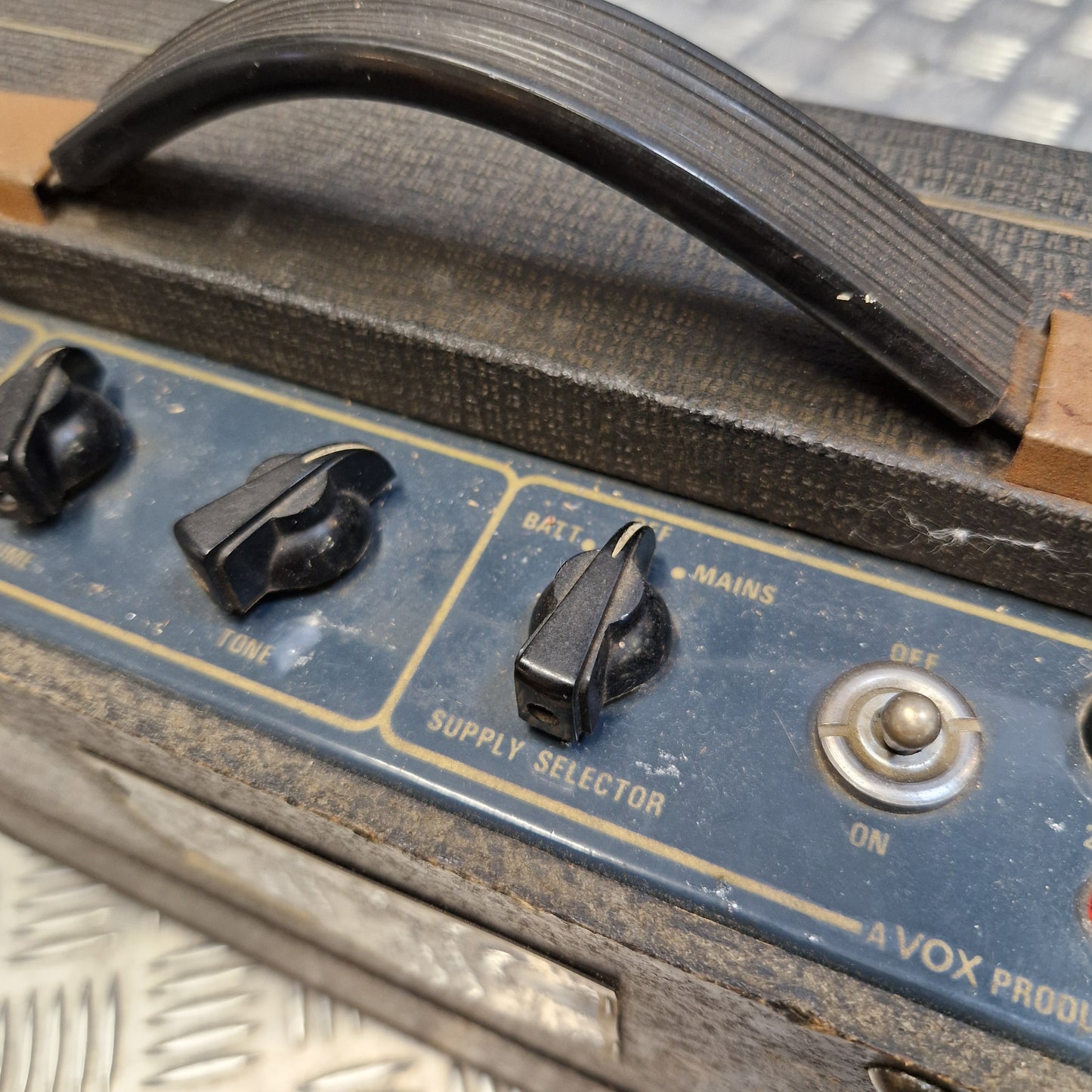 Pre-Owned Vox Escort Close-up of the control panel of a vintage Vox amplifier, showing black knobs, a blue faceplate with gold lettering, and a black handle on a weathered wooden body.