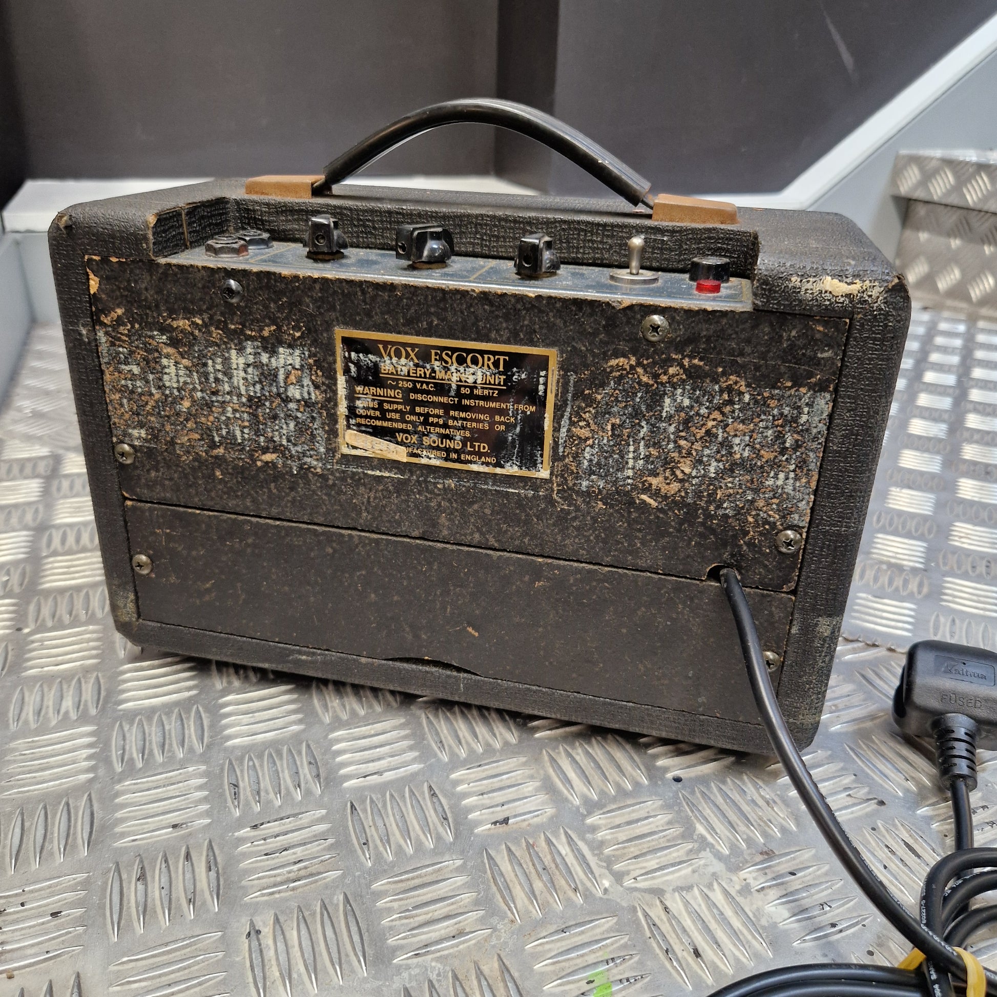 Pre-Owned Vox Escort A vintage Marshall amp head with a heavily worn, rusted black canvas cover, sitting on a diamond plate metal surface. The front features a gold-colored Marshall logo plate, black knobs, and a black carrying handle.