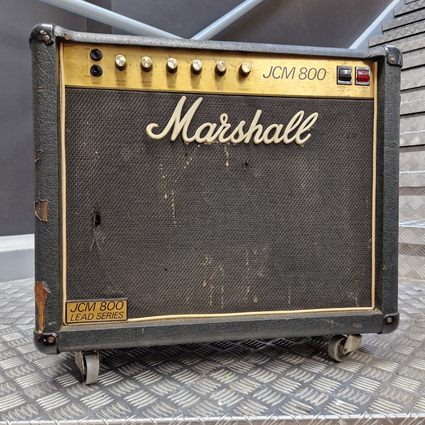 Pre-Owned Marshall JCM 800 A vintage Marshall JCM 800 LF0D Series guitar amplifier head, featuring a black textured grille cloth with a cream-colored Marshall logo, gold trim, and control knobs on the left side, resting on a diamond plate metal surface.