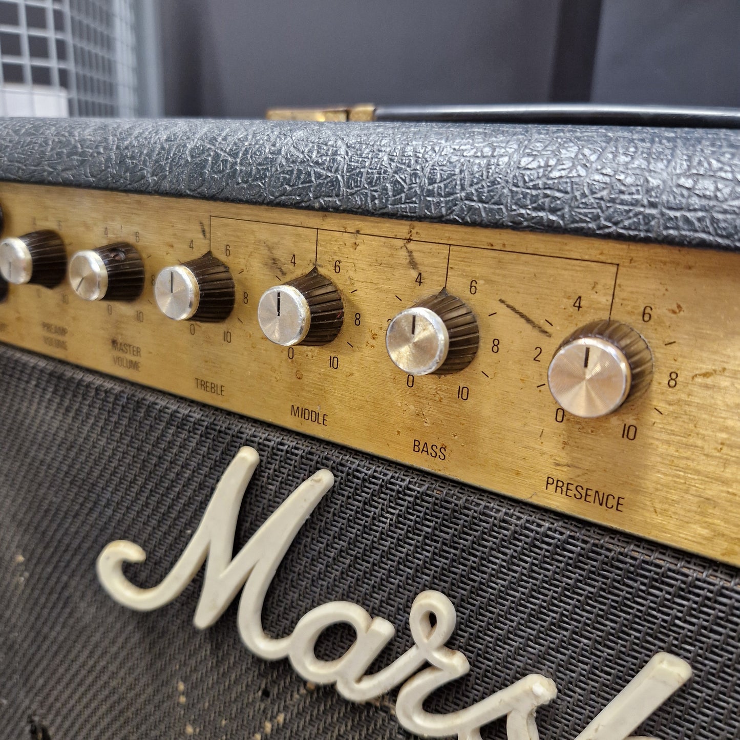 Pre-Owned Marshall JCM 800 Close-up of a Marshall amplifier control panel with silver dials on a gold-tone plate, next to a black textured grille with white Marshall script.