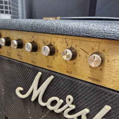 Pre-Owned Marshall JCM 800 Close-up of a Marshall amplifier control panel with silver dials on a gold-tone plate, next to a black textured grille with white Marshall script.