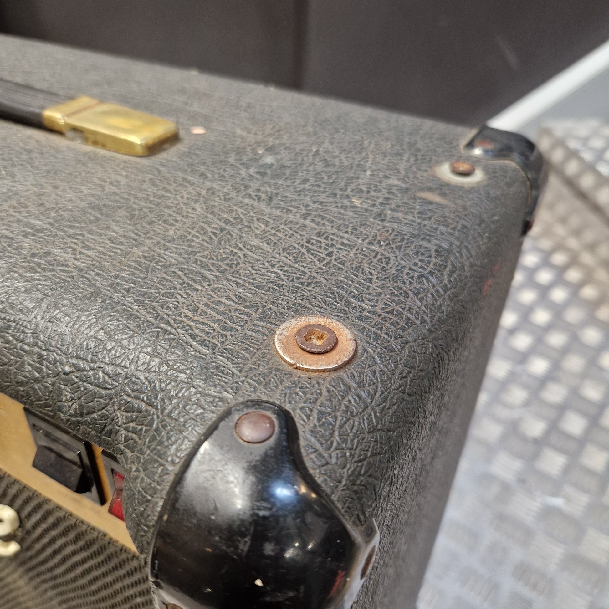 Pre-Owned Marshall JCM 800 Close-up of the corner of a black textured guitar amplifier or speaker cabinet with a glossy black corner piece and brass hardware.
