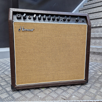 Pre-Owned Hartwood HW-AA-30 A vintage-style Harman guitar amplifier with a brown wood-look cabinet, tan woven grille cloth, and black control knobs, photographed from above on a textured metal surface.