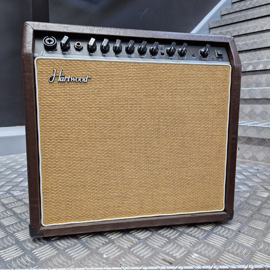 Pre-Owned Hartwood HW-AA-30 A vintage-style Harman guitar amplifier with a brown wood-look cabinet, tan woven grille cloth, and black control knobs, photographed from above on a textured metal surface.
