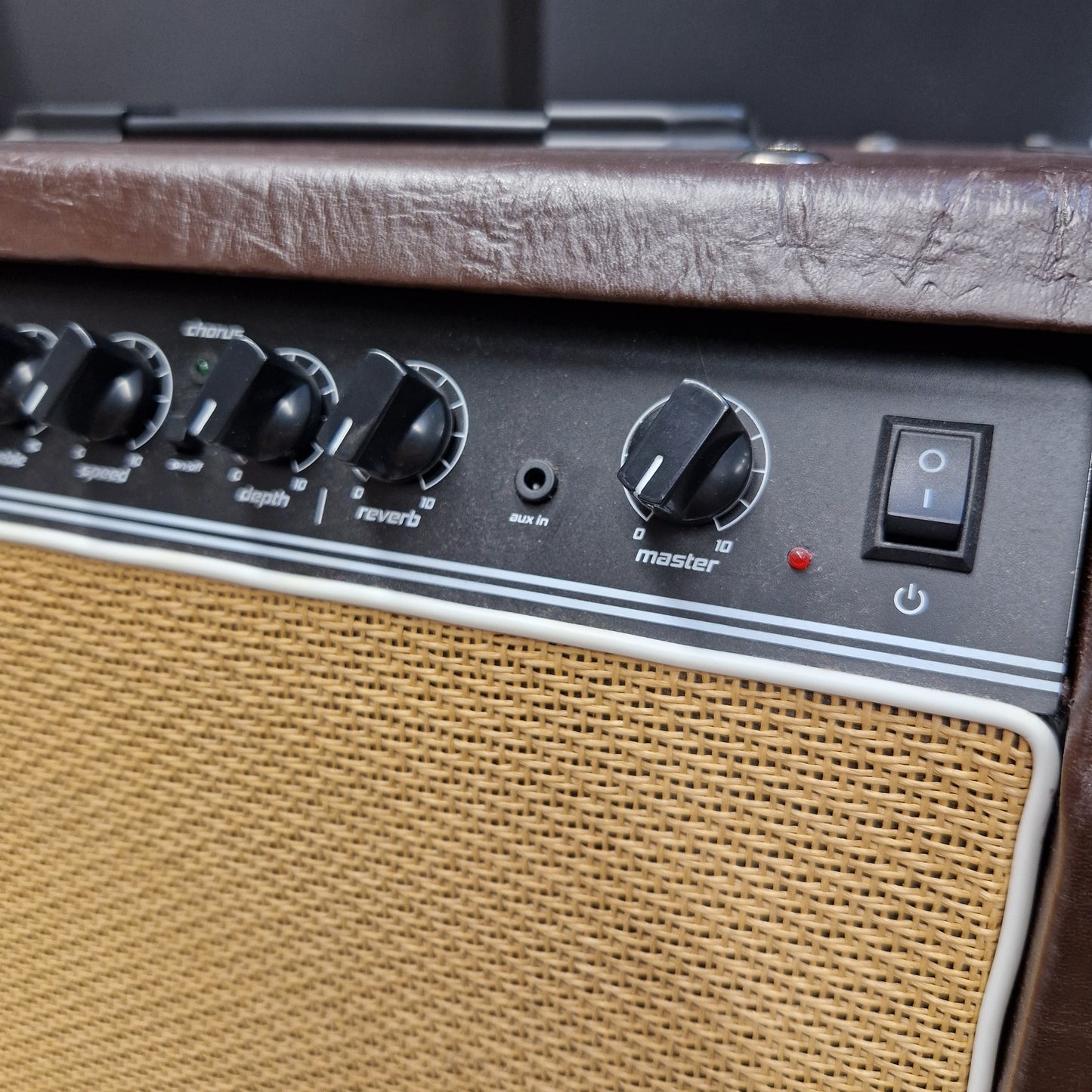 Pre-Owned Hartwood HW-AA-30 Close-up of an amplifier control panel with black knobs, a power switch, and a tan mesh grille on a brown textured cabinet.