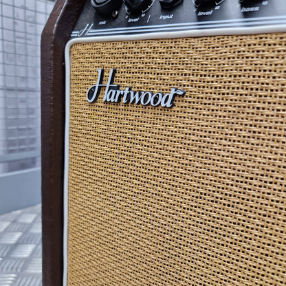 Pre-Owned Hartwood HW-AA-30 Close-up of a vintage-style Hartwood amplifier speaker grille in tan mesh with a silver script logo, showing part of the dark wood cabinet and control knobs on the left.