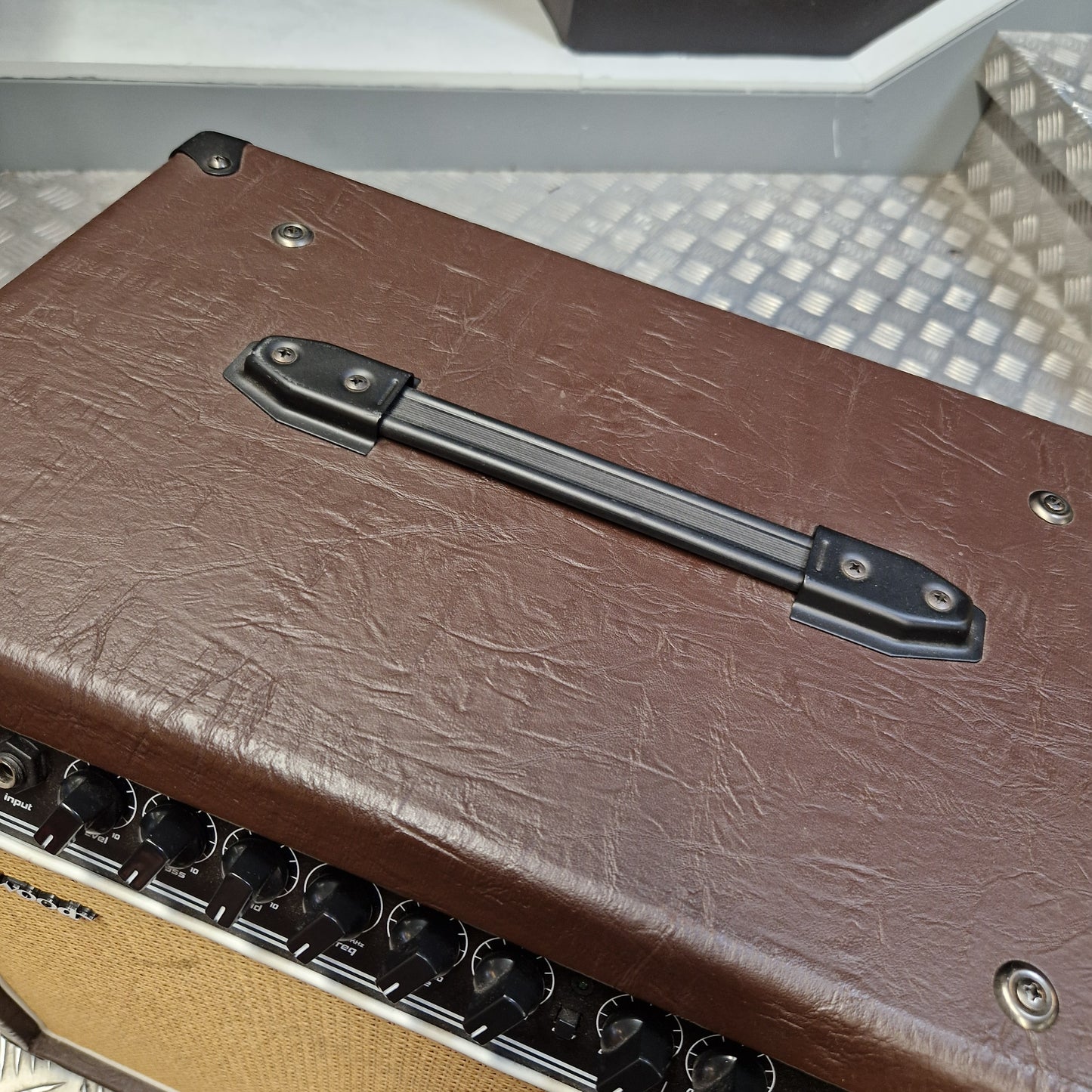 Pre-Owned Hartwood HW-AA-30 Close-up of the side of a brown textured amplifier or speaker cabinet with a black handle, metal screws, and part of the tan speaker grille visible.