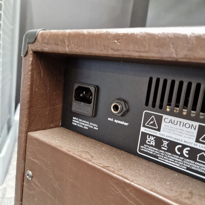 Pre-Owned Hartwood HW-AA-30 Close-up of the rear power and audio port area of a brown textured speaker or amplifier, showing a black back panel with a 3-pin power inlet, a 3.5mm jack, ventilation slots, and a warning label.