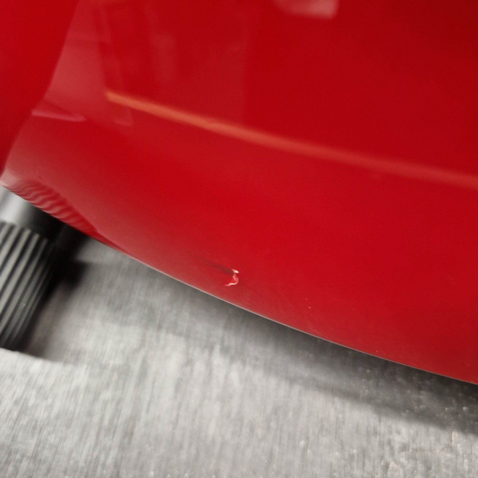 Pre-Owned Squier MIK 1992 Close-up of a glossy red curved surface, likely a vehicle body panel or wheel well, adjacent to a textured gray metal surface.