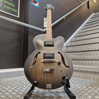 Pre-Owned Ibanez AF55-TKF Hollowbody Electric - Black Flat A dark brown hollow-body electric guitar with a metallic finish, mounted on a black stand in a showroom with a staircase in the background.