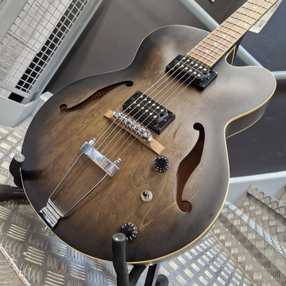 Pre-Owned Ibanez AF55-TKF Hollowbody Electric - Black Flat A double-cutaway electric guitar with a dark brown sunburst finish, featuring black pickups, chrome hardware, and a maple neck, resting on a metal stand.