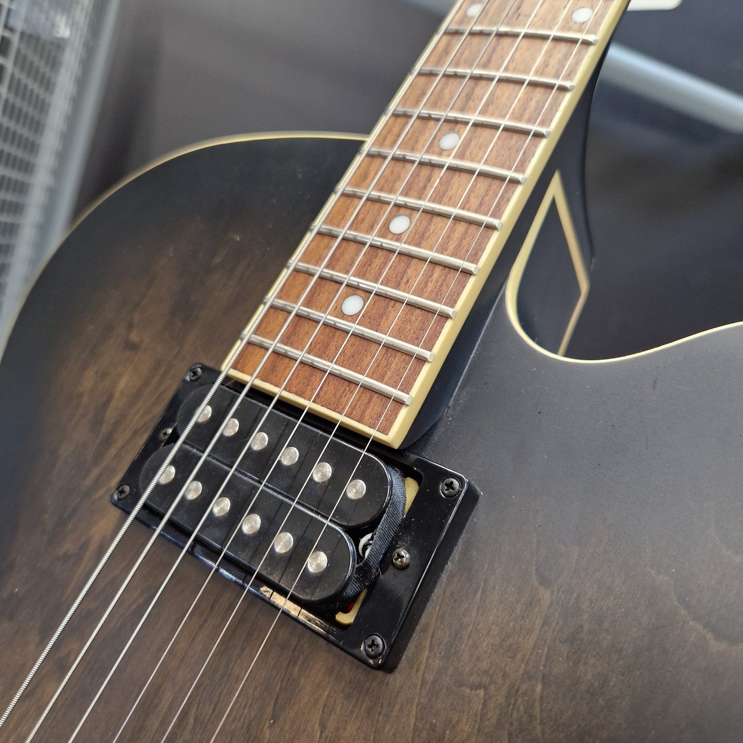 Pre-Owned Ibanez AF55-TKF Hollowbody Electric - Black Flat Close-up of an electric guitar body and neck, showing a dark brown to black sunburst finish, a black humbucker pickup with silver pole pieces, and a maple fretboard with white dot inlays.