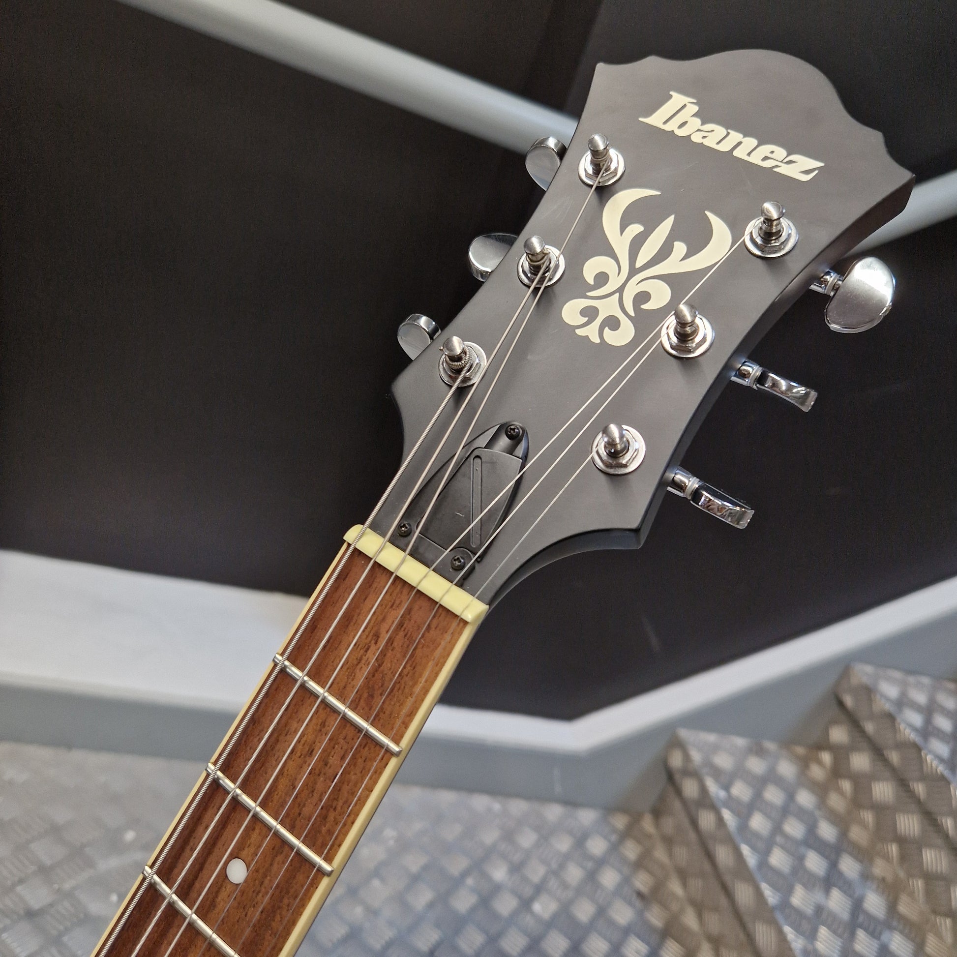 Pre-Owned Ibanez AF55-TKF Hollowbody Electric - Black Flat Close-up of an Ibanez acoustic guitar headstock and neck, showing the black headstock with gold Ibanez logo, tuning pegs, and a brown wood fretboard.
