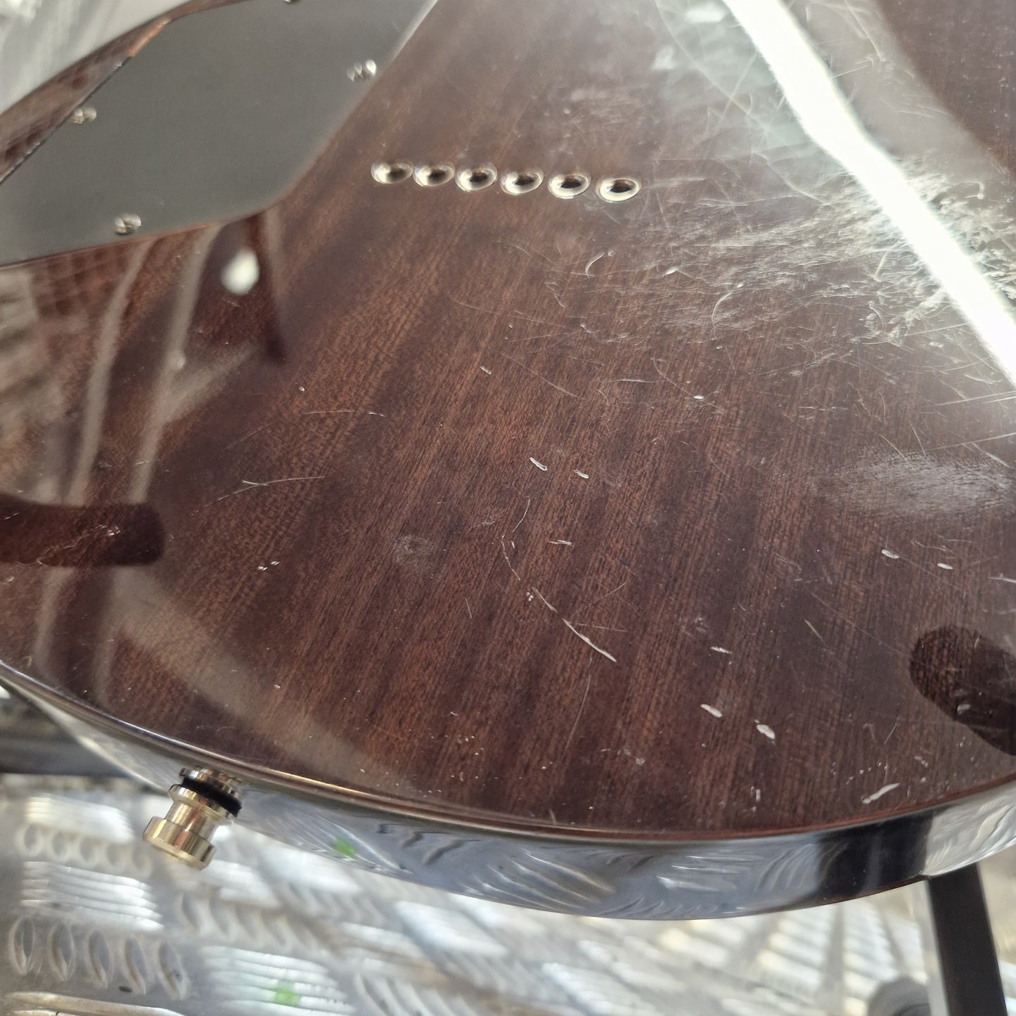Pre-Owned Chapman ML-2 Electric - Grey Close-up of a dark brown wood-grain guitar body with visible scratches, a metal hardware piece, and a small gold-toned control knob.