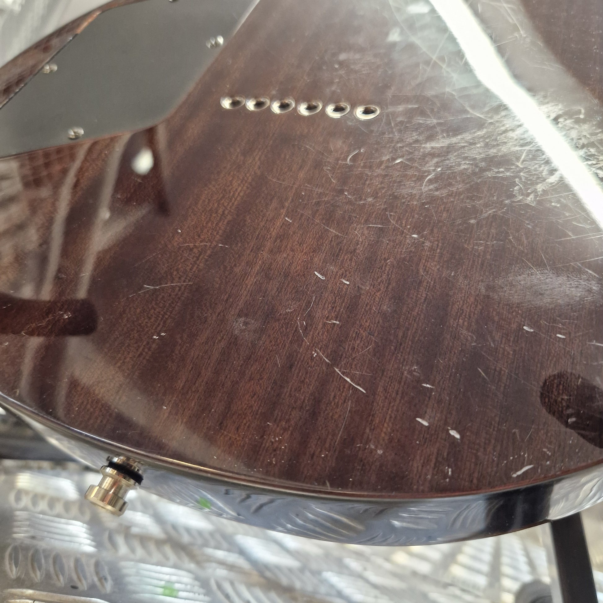 Pre-Owned Chapman ML-2 Electric - Grey Close-up of a dark brown wood-grain guitar body with visible scratches, a metal hardware piece, and a small gold-toned control knob.