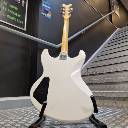 Pre-Owned Schecter Shaun Morgan Signature Electric - White A white electric guitar shown from the back on a stand, with a light wood neck and black pickguard, photographed in an indoor setting with stairs and a dark wall in the background.