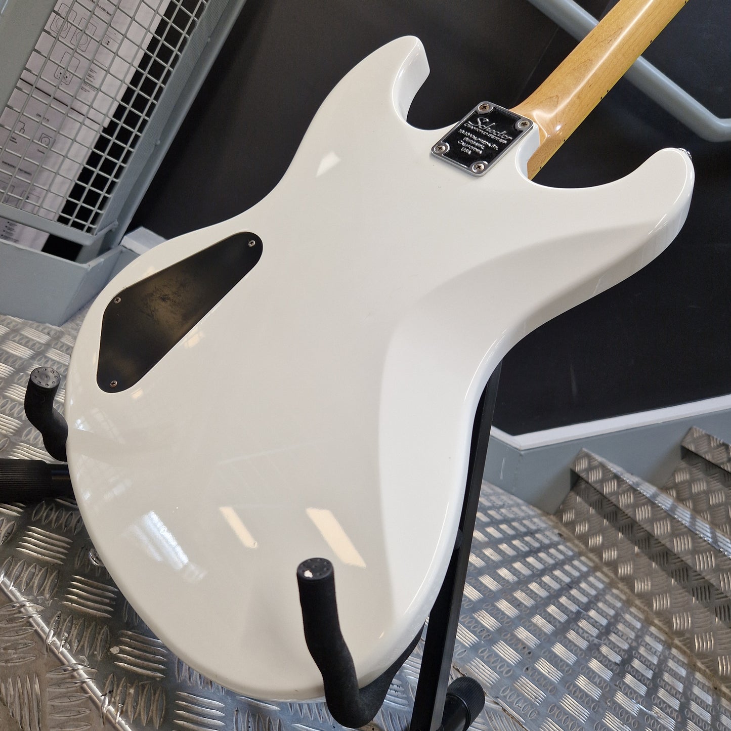 Pre-Owned Schecter Shaun Morgan Signature Electric - White Close-up of the glossy white back side of an electric guitar resting on a stand, with part of the natural wood neck visible and a black pickguard.