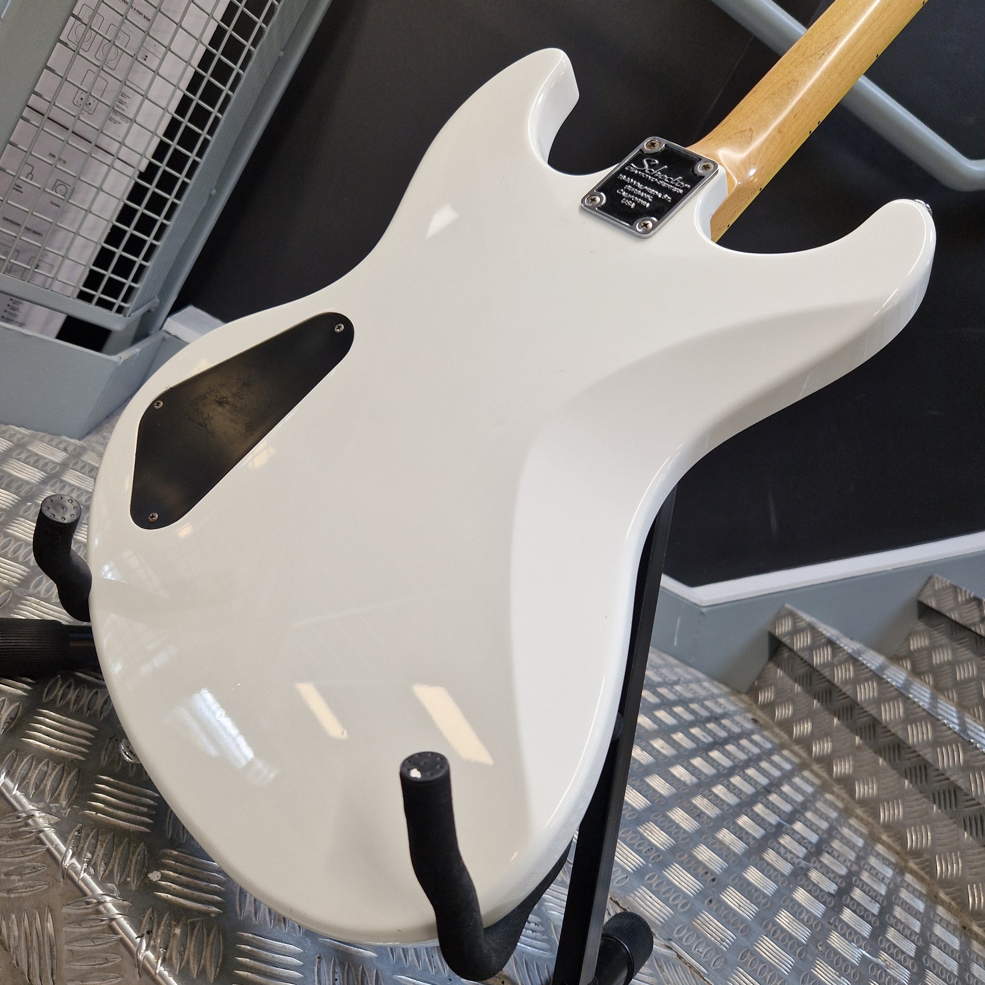 Pre-Owned Schecter Shaun Morgan Signature Electric - White Close-up of the glossy white back side of an electric guitar resting on a stand, with part of the natural wood neck visible and a black pickguard.