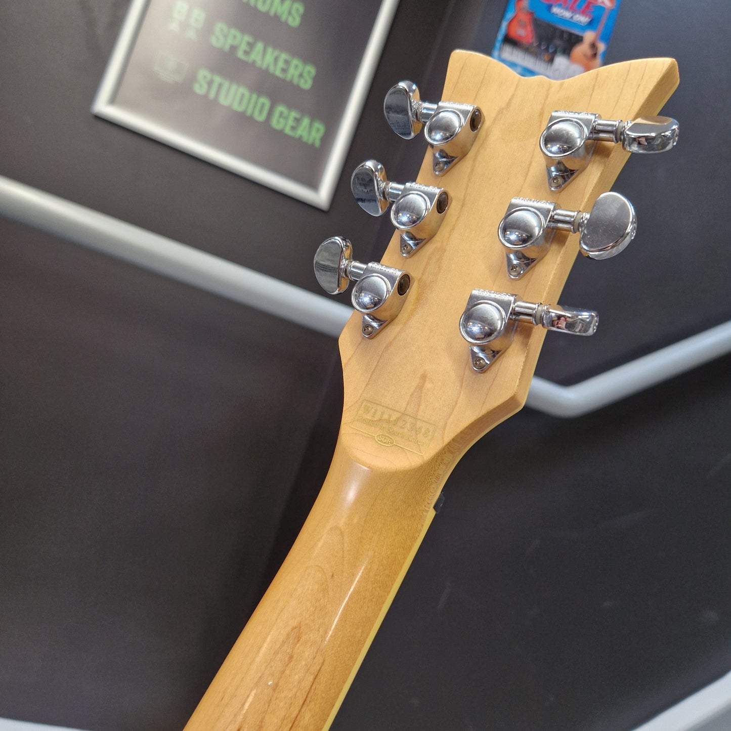 Pre-Owned Schecter Shaun Morgan Signature Electric - White Close-up of the headstock of a guitar, showing six silver tuning pegs and a light natural wood neck against a dark display background.