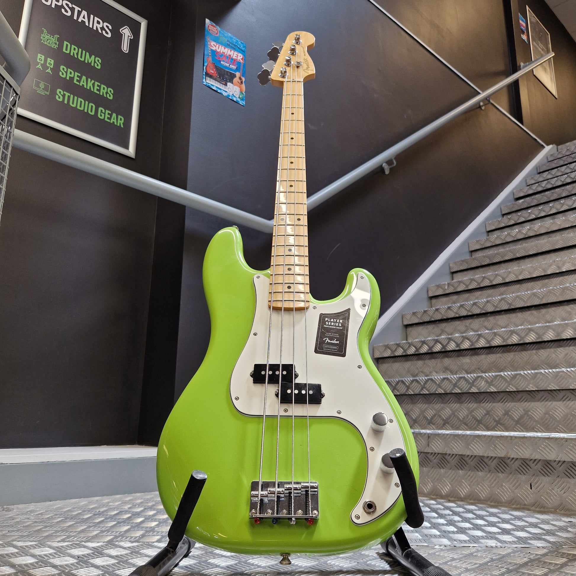 Pre-Owned Fender Player Precision Bass - Limited Edition Electron Green A bright lime green electric bass guitar with a maple neck and white pickguard, hanging on a stand in a store or studio setting.