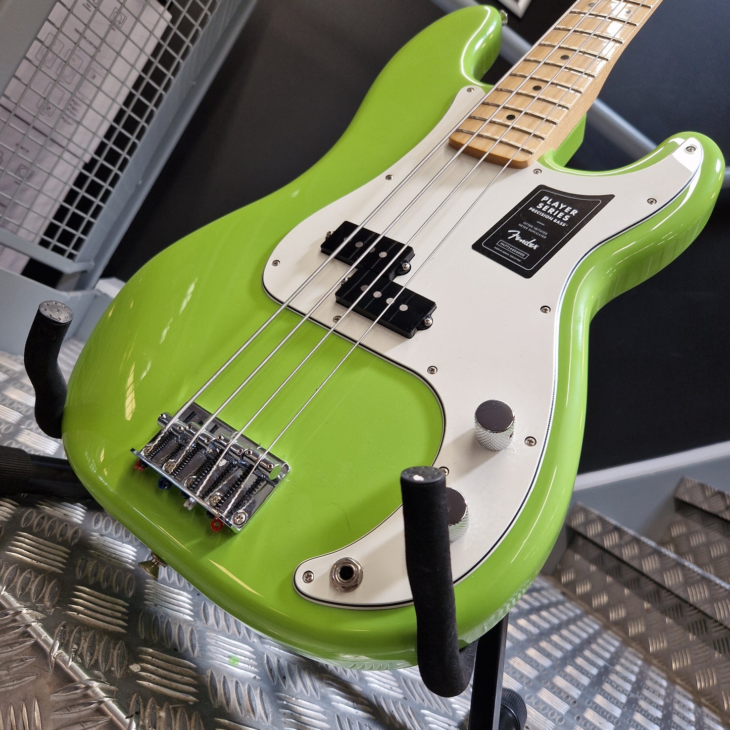 Pre-Owned Fender Player Precision Bass - Limited Edition Electron Green A close-up of a bright lime green electric bass guitar with a white pickguard, resting on a stand in what appears to be a shop or studio setting.