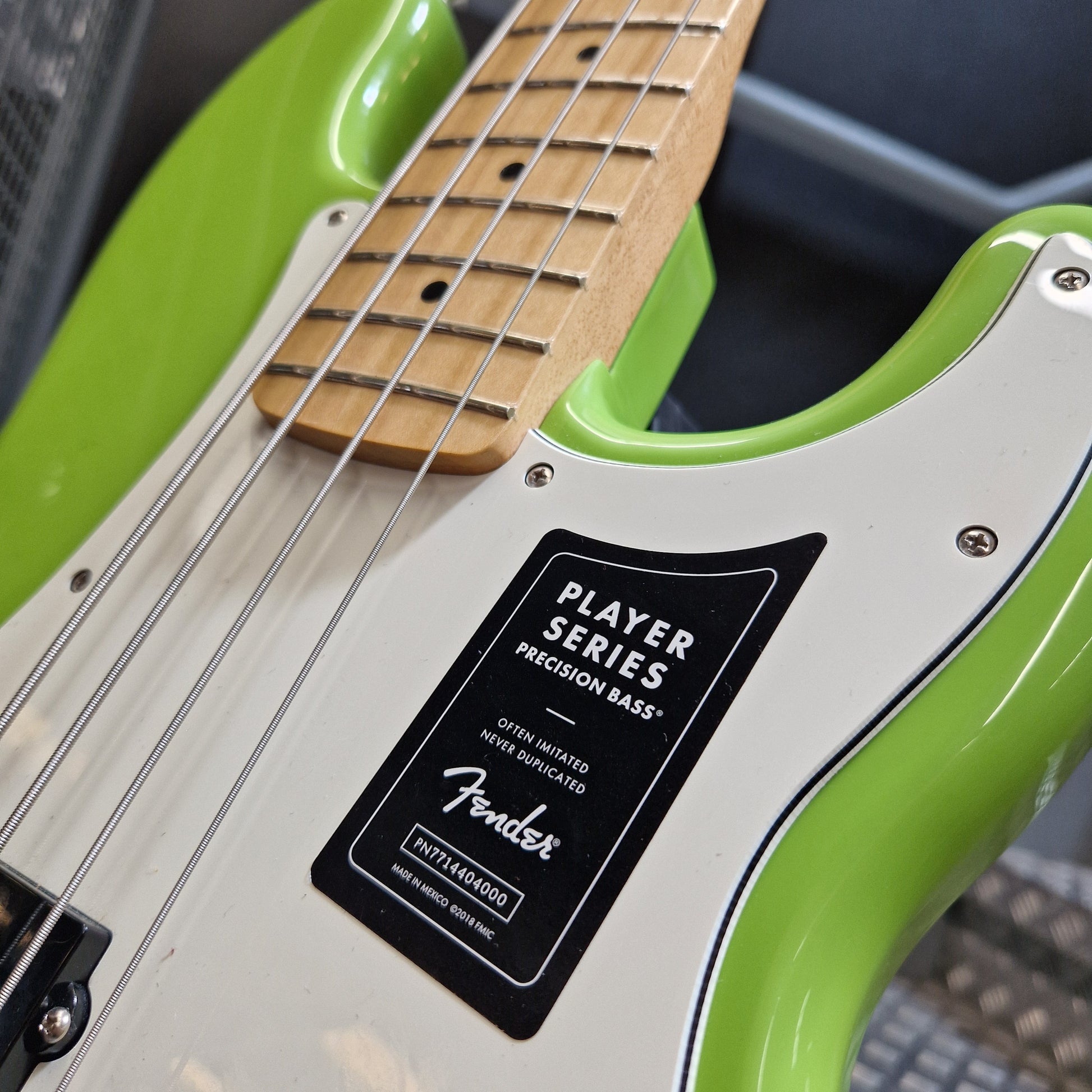 Pre-Owned Fender Player Precision Bass - Limited Edition Electron Green Close-up of a Fender Player Series Precision Bass electric guitar body in lime green and white, showing the black Fender logo badge and part of the natural wood fretboard.