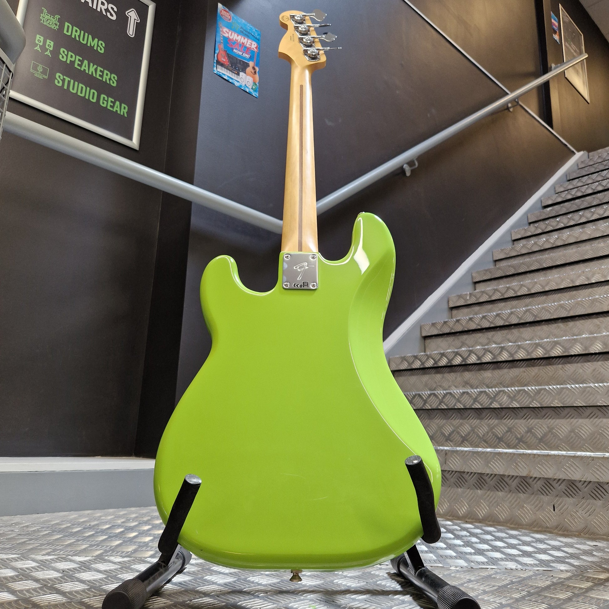 Pre-Owned Fender Player Precision Bass - Limited Edition Electron Green A bright lime green electric bass guitar with a natural wood neck, displayed on a black stand inside what appears to be a showroom or studio.