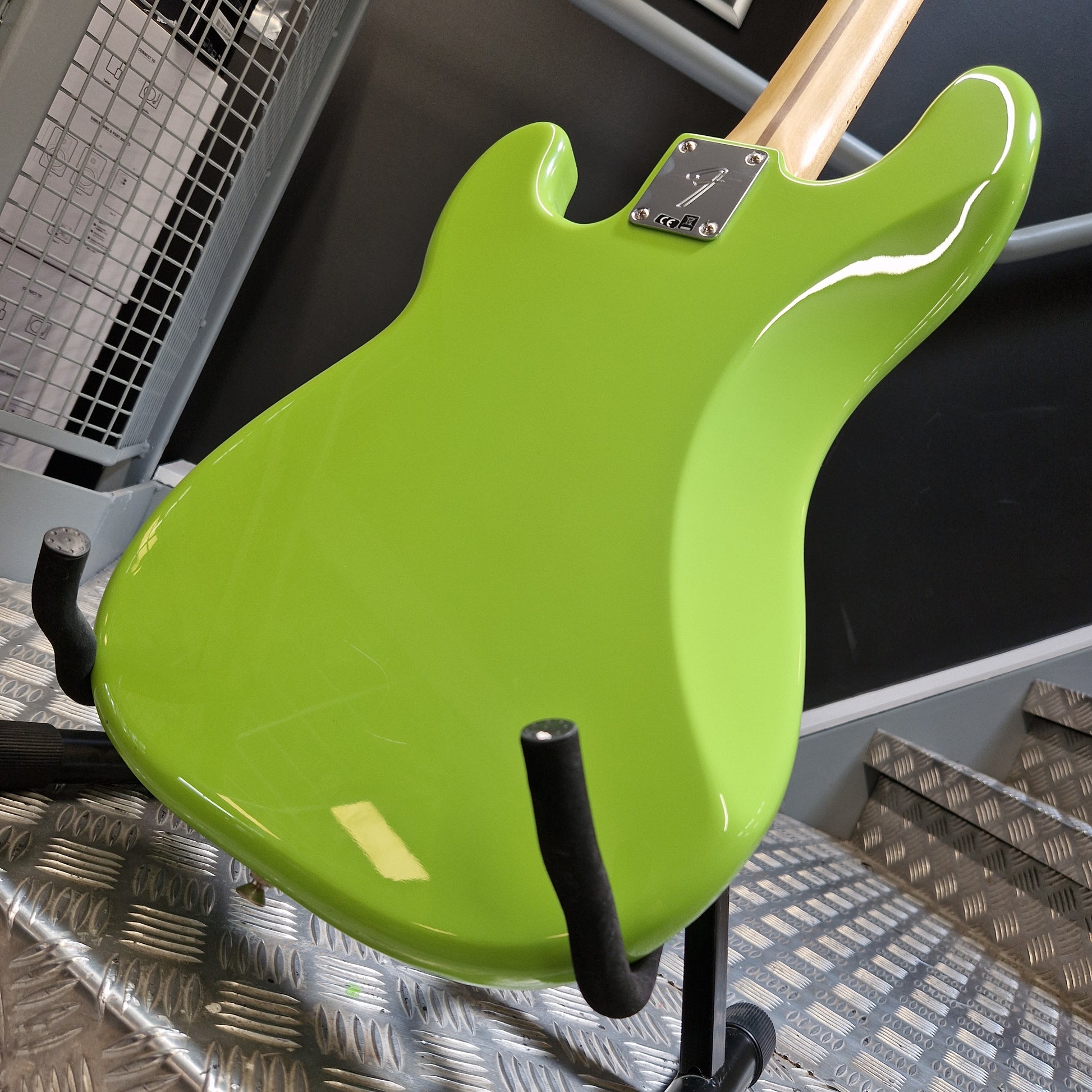 Pre-Owned Fender Player Precision Bass - Limited Edition Electron Green Close-up of the back body of a bright lime green electric guitar mounted on a black stand, with part of the light wood neck and a metal control plate visible.