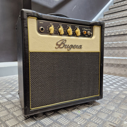 Pre-Owned Bugera Vintage 5 V5 Valve Guitar Combo A Bugga guitar amplifier head photographed from above, resting on a dark surface against a textured diamond-plate metal wall. The amp has a black body, a cream-colored faceplate, and gold controls and trim.