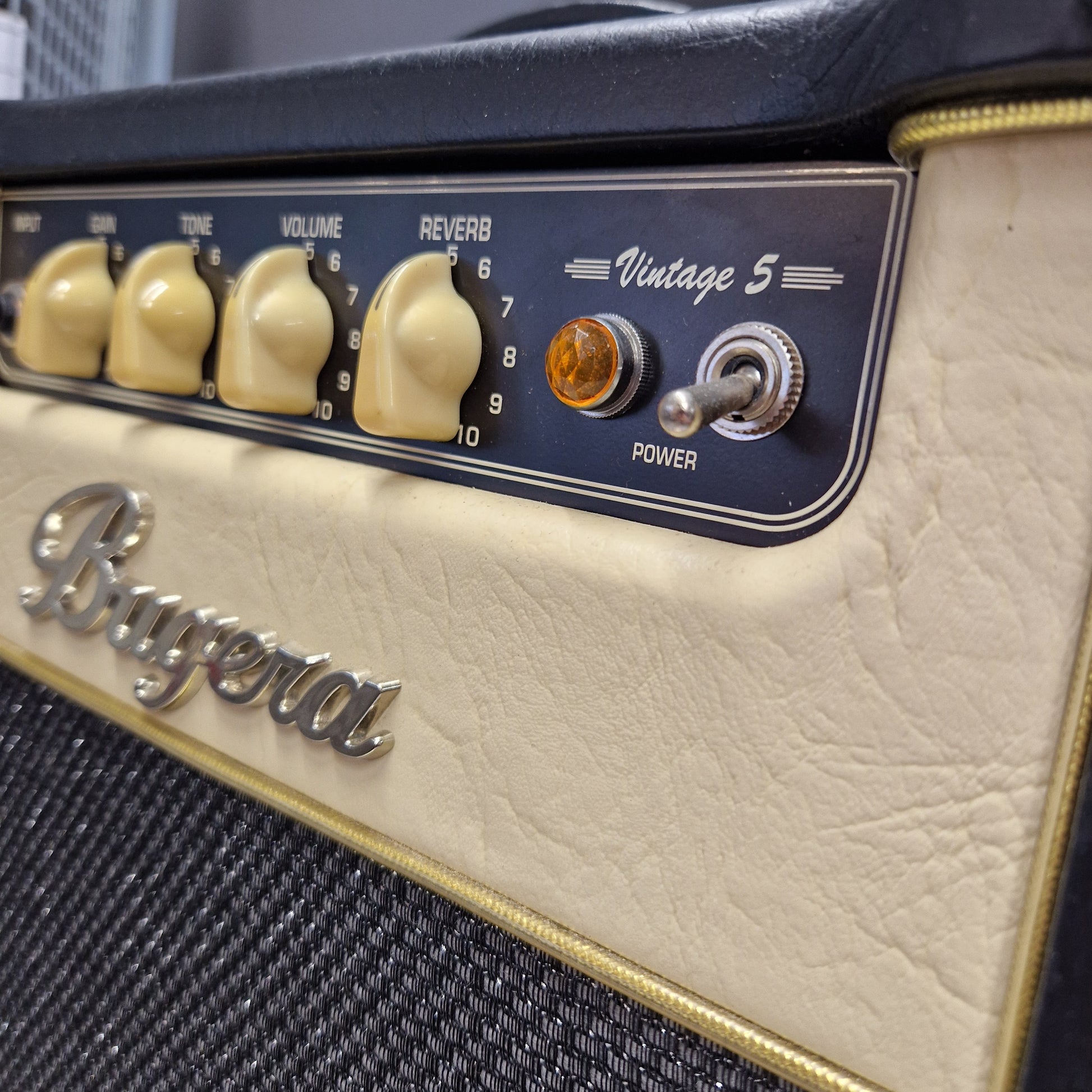 Pre-Owned Bugera Vintage 5 V5 Valve Guitar Combo Close-up of a vintage-style guitar or amplifier control panel with cream-colored textured faceplate, black mesh grille, gold trim, cream knobs, and a silver 'Burgal' logo.