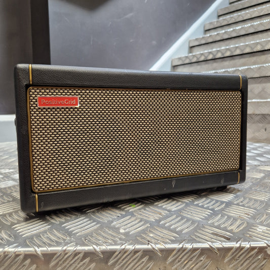 Pre-Owned Positive Grid Spark 40-Watt Smart Guitar Combo & Bluetooth Speaker A portable speaker with a black textured leather-like body, a beige mesh grille, and a small red 'Portable' logo badge, resting on a diamond plate metal surface.