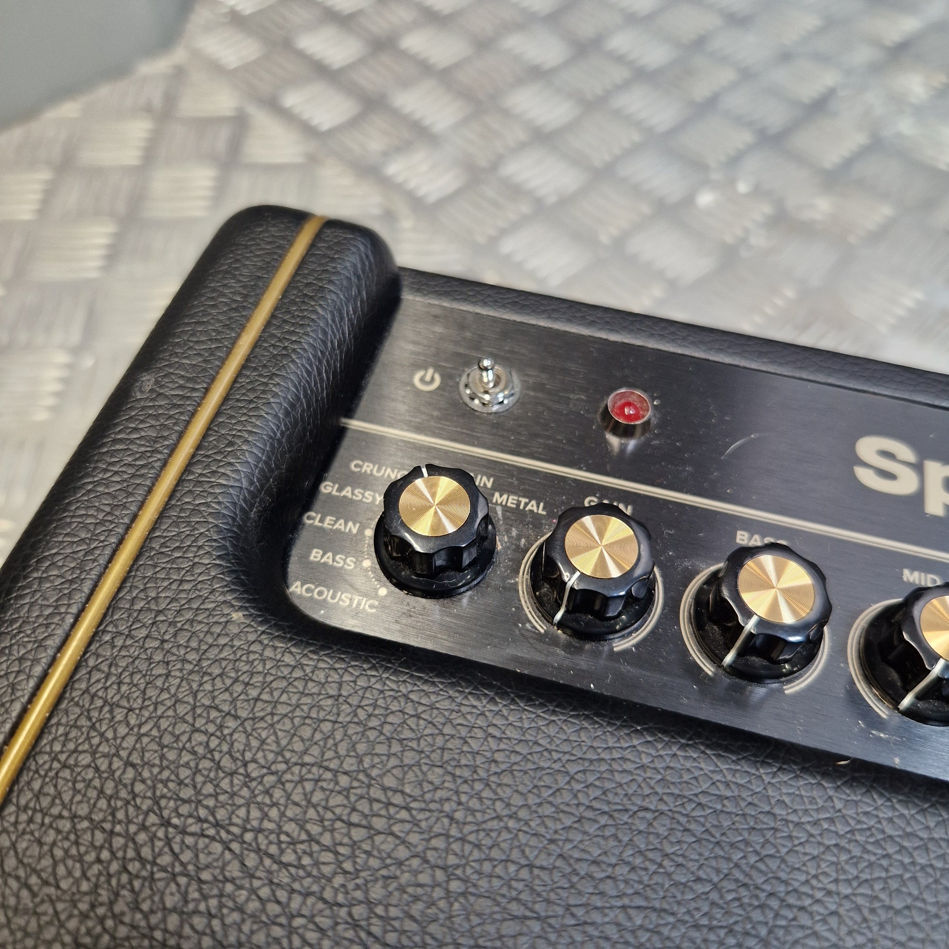 Pre-Owned Positive Grid Spark 40-Watt Smart Guitar Combo & Bluetooth Speaker Close-up of a black guitar amplifier control panel with gold-tone knobs, a red indicator light, and a silver switch on a textured black leather body.