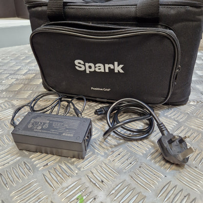 Pre-Owned Positive Grid Spark 40-Watt Smart Guitar Combo & Bluetooth Speaker A black Spark Positive Color portable light bag shown with its power adapter and UK plug on a diamond plate metal surface.