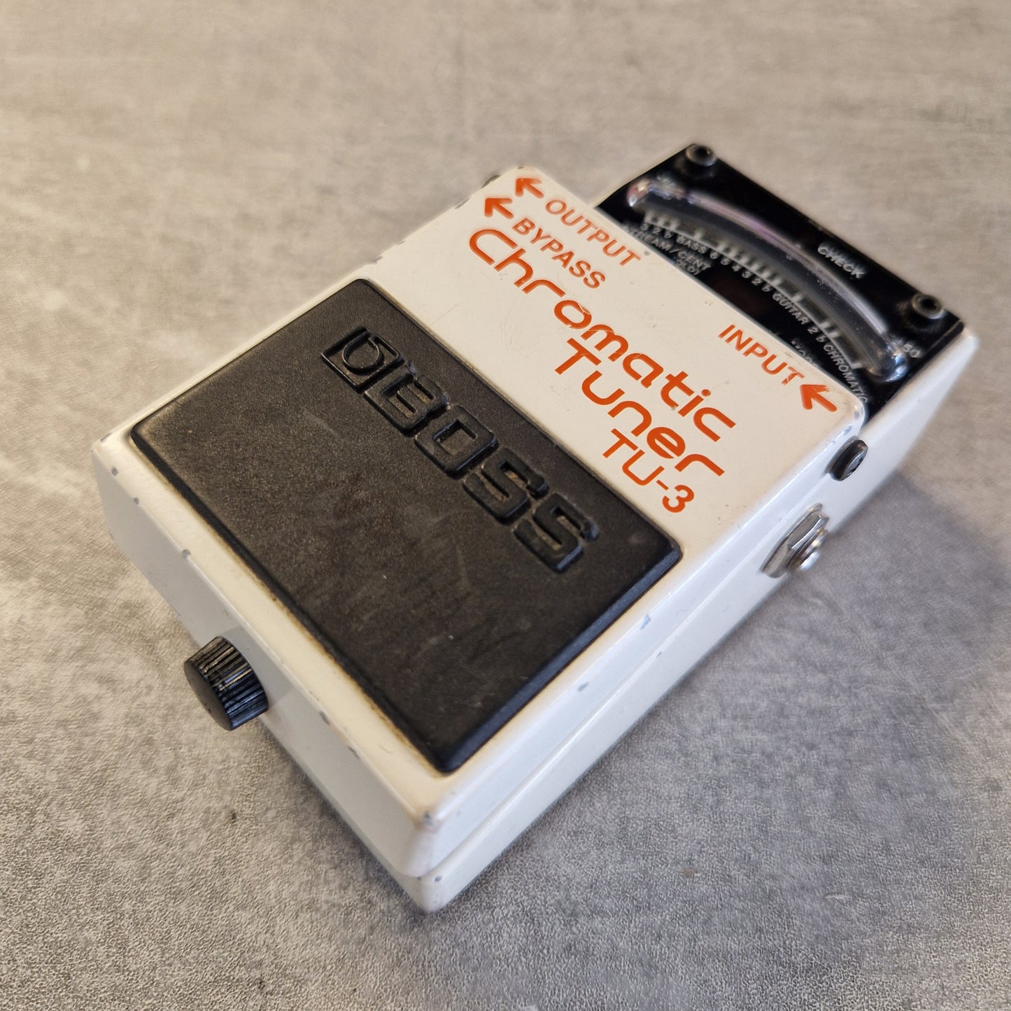 Pre-Owned Boss TU-3 Tuner Pedal A vintage BOSS TU-3 Chromatic Guitar Tuner pedal, featuring a white metal casing with orange lettering and a black footswitch, resting on a gray textured surface.
